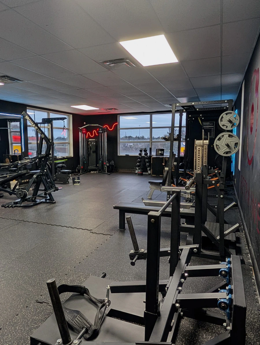 Free-weight floor at Retraine with rigs, dumbbells and a press station.