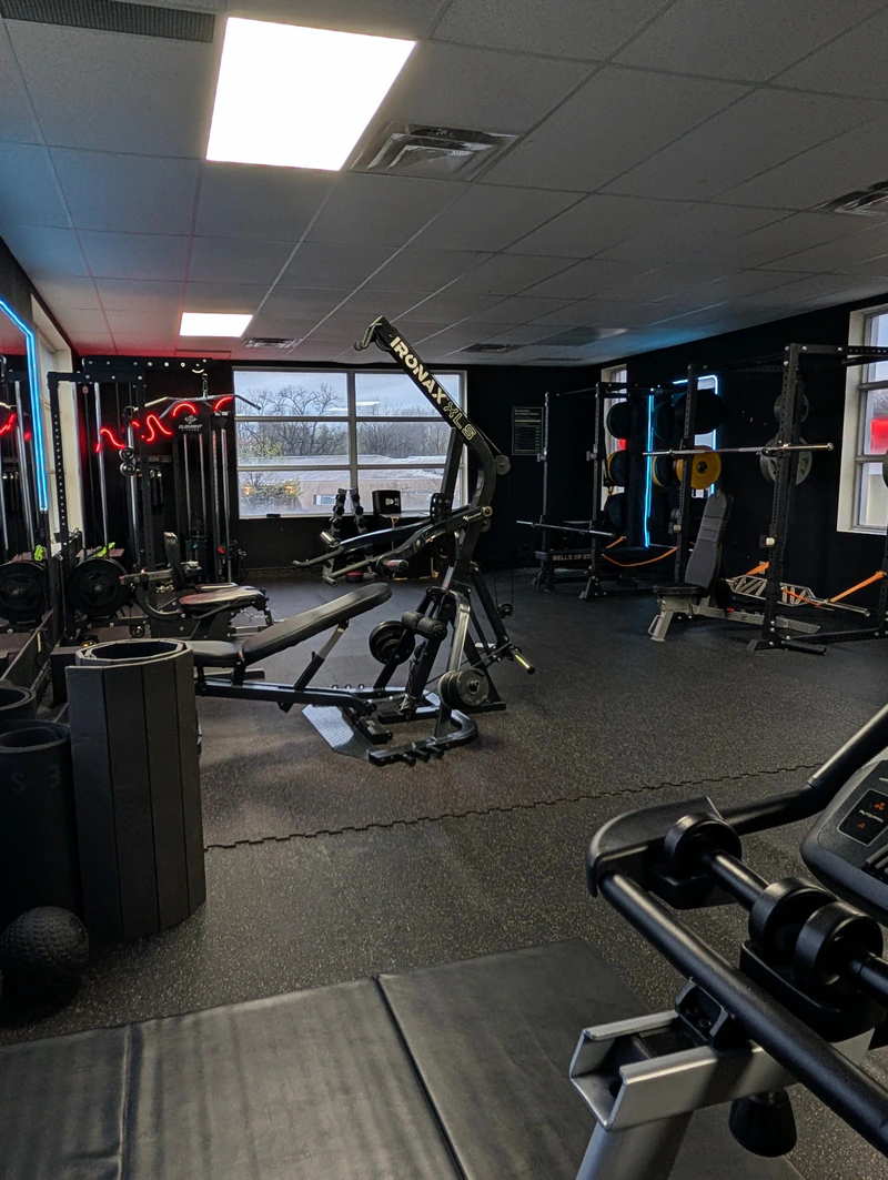 Plate-loaded machines and squat racks at Retraine in Pickering under blue and red neon, set up for high-frequency training.