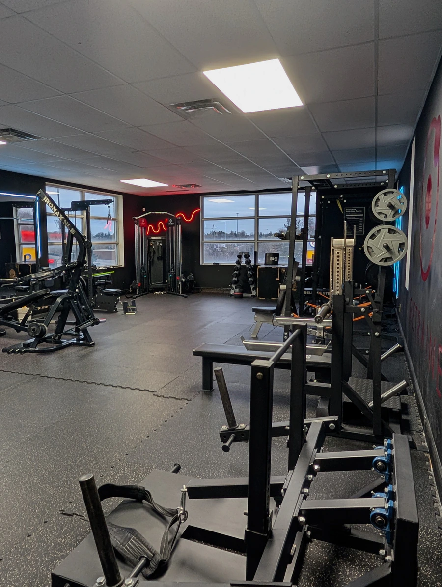 Squat and bench area at Retraine in Pickering with loaded racks, leg-press station and red neon by the windows.